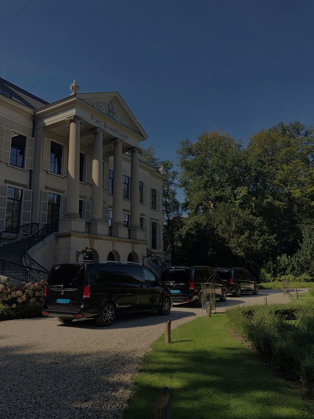 Black vans waiting on the drive of a classical country house